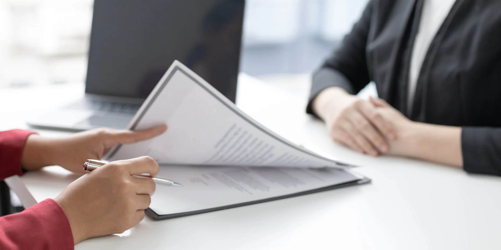 Close-up view of a candidate handing a resume to an interviewer at a desk.