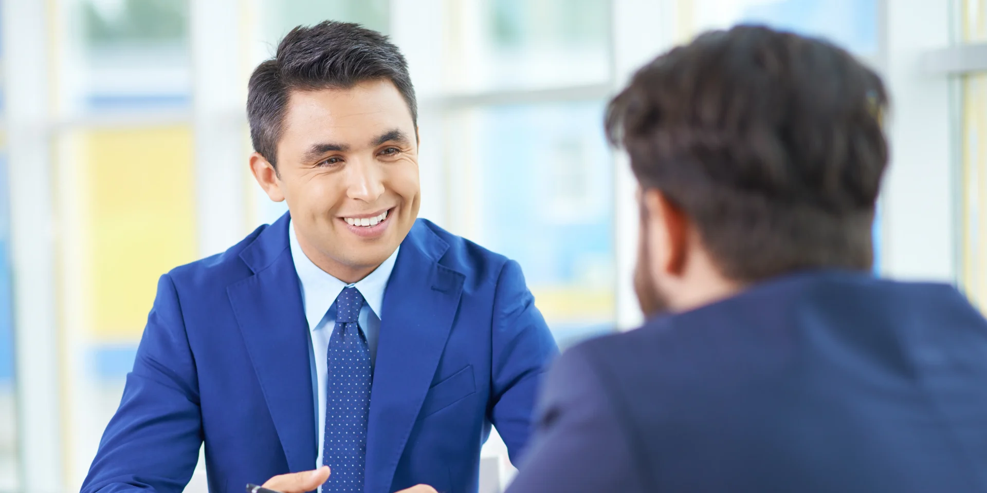 A smiling man in a blue suit engaged in a one-on-one interview with another man.