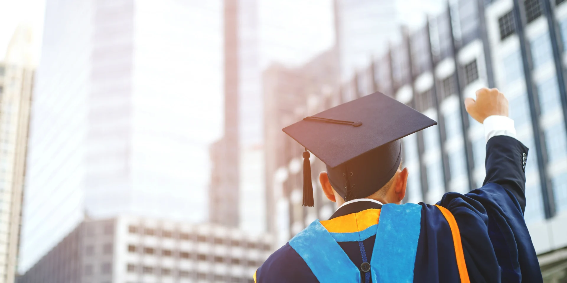 From Graduation to Career: Own Your Next Chapter Graduate in academic regalia raising a fist in triumph in front of modern buildings.