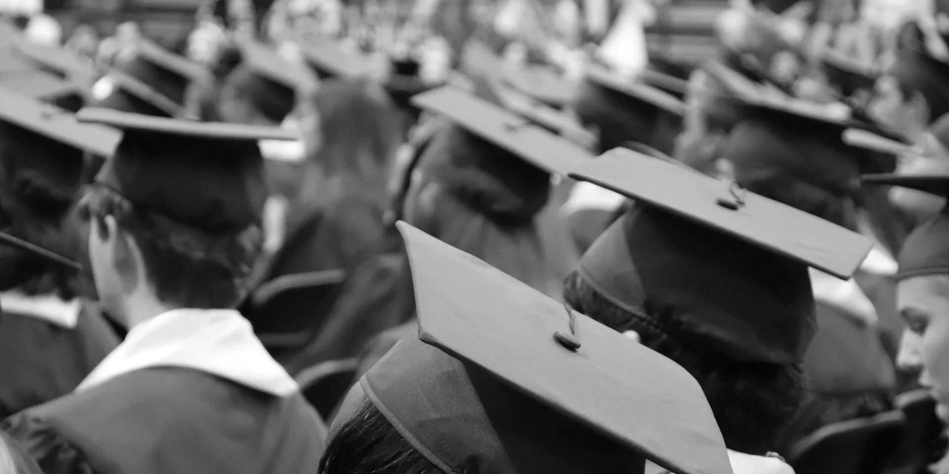 Black and white image of graduates wearing caps during a commencement ceremony.
