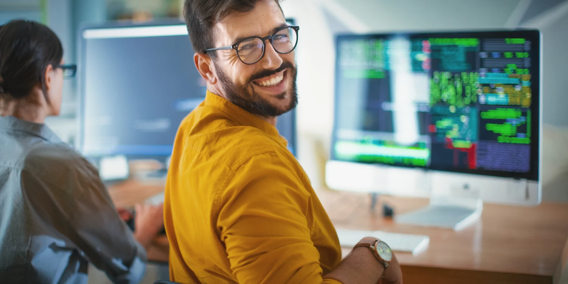 From Nervous Candidate to Confident Colleague | Professional Interview Prep A confident and happy male software developer with glasses smiling over his shoulder while working in a modern office with code on his computer screen.
