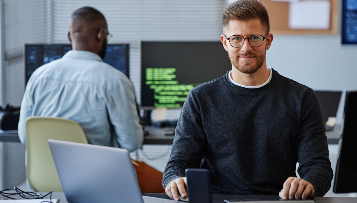 Focused professional typing at a workstation with multiple monitors displaying code and technical data.