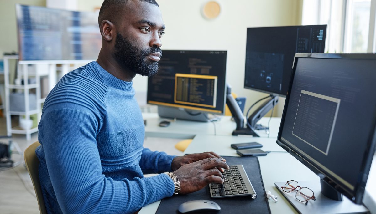 Presenting Confidence in Technical and Behavioral IT Interviews Smiling professional wearing glasses working at a computer in an office with coding screens in the background.