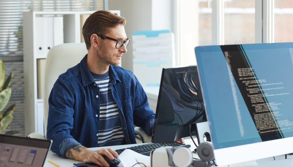 Professional software developer working at a computer with multiple monitors displaying code.